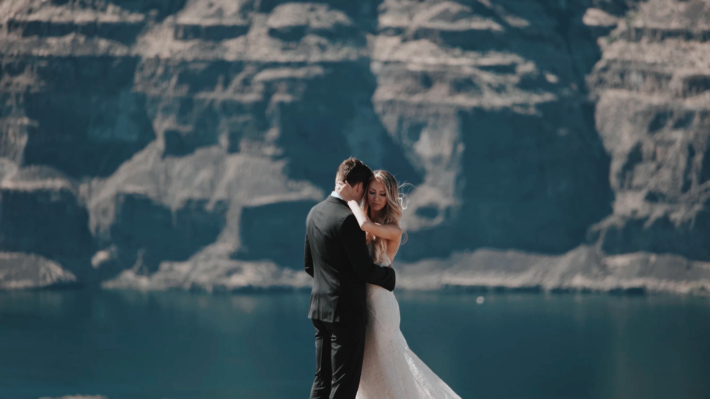 A newly married couple embracing beside a mountain lake and cliff