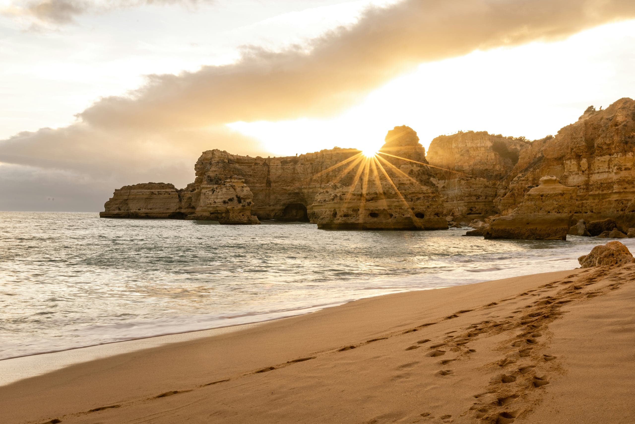Low sun spilling through the ochre sea cliffs onto Praia da Marinha in the Algarve
