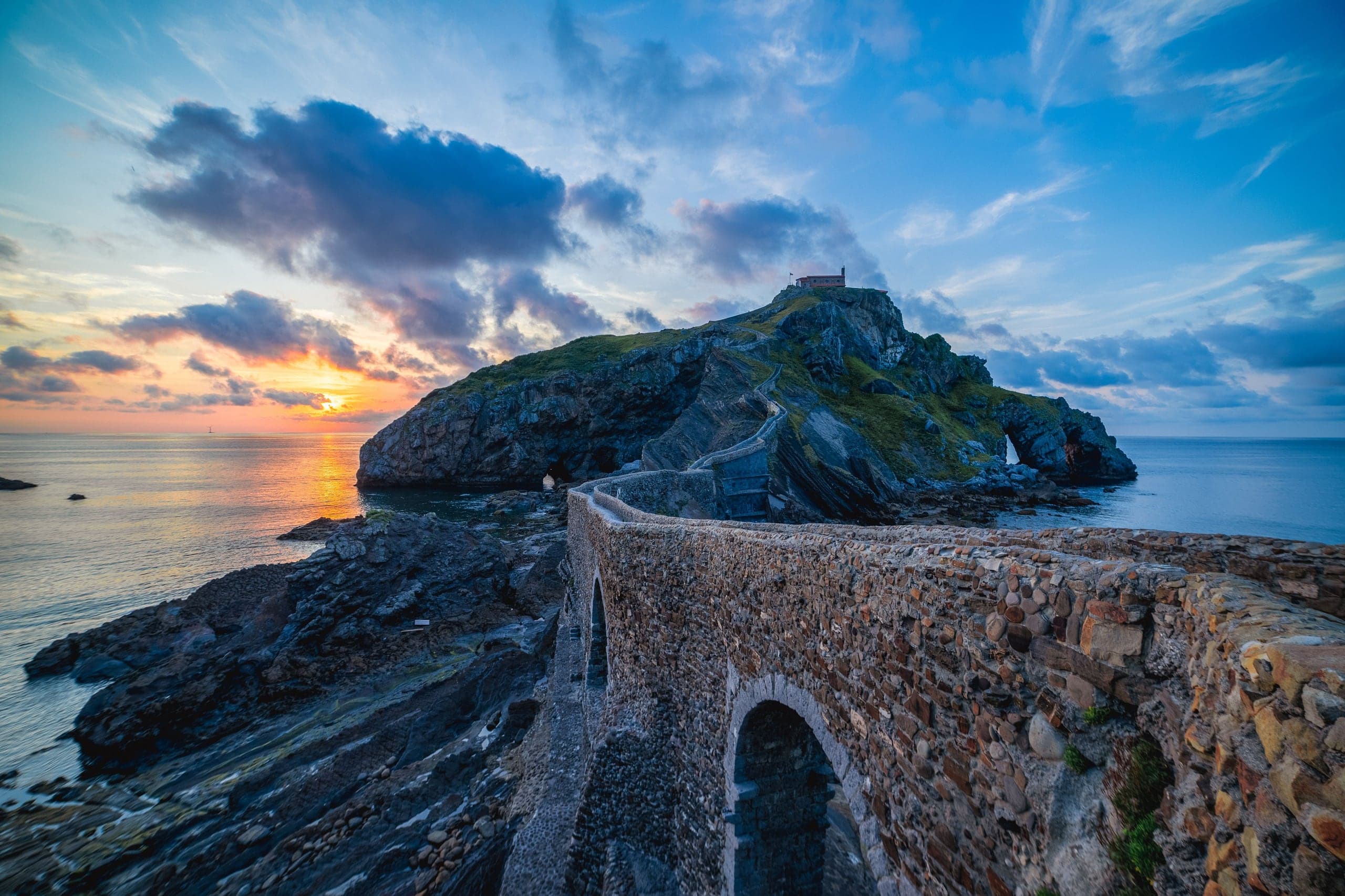 The stone causeway curling toward San Juan de Gaztelugatxe as sunset burns across the Basque sea