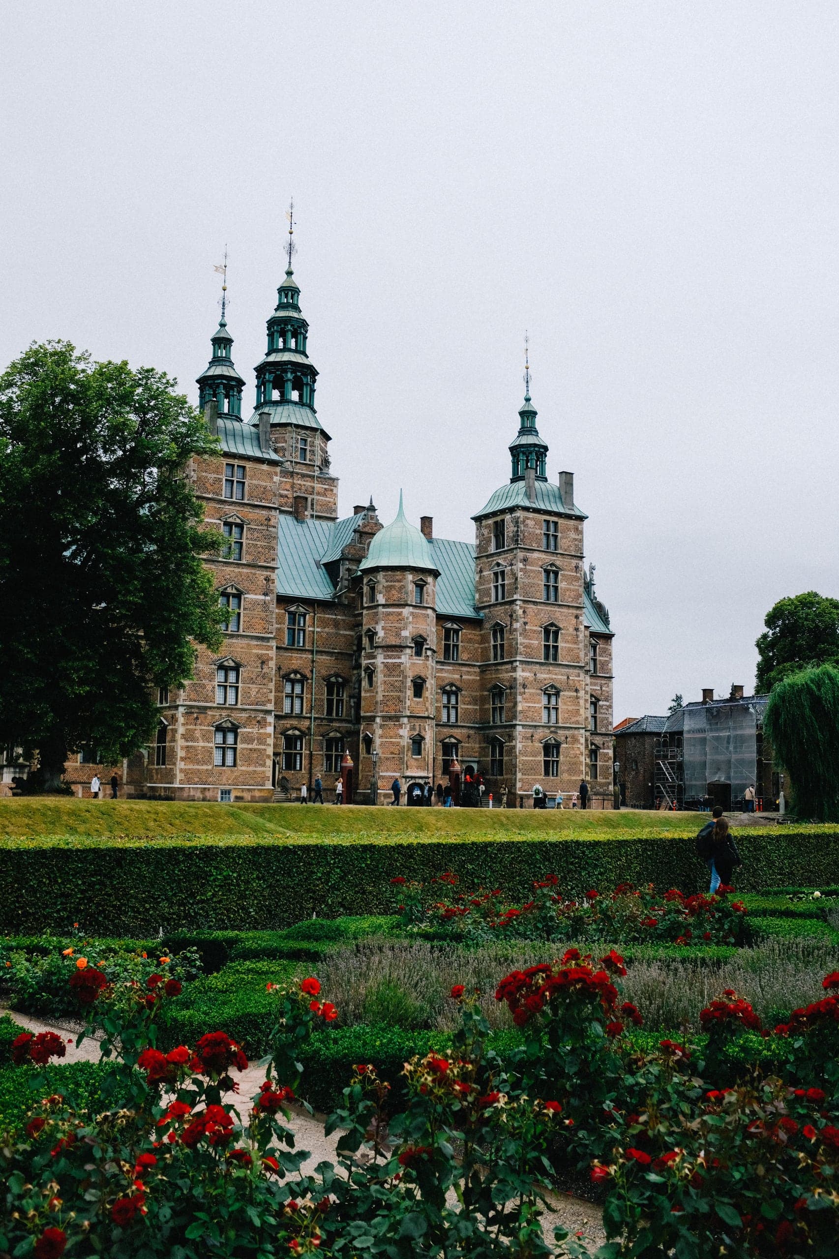 Rosenborg Castle rising behind clipped hedges and deep red roses in Copenhagen's King's Garden