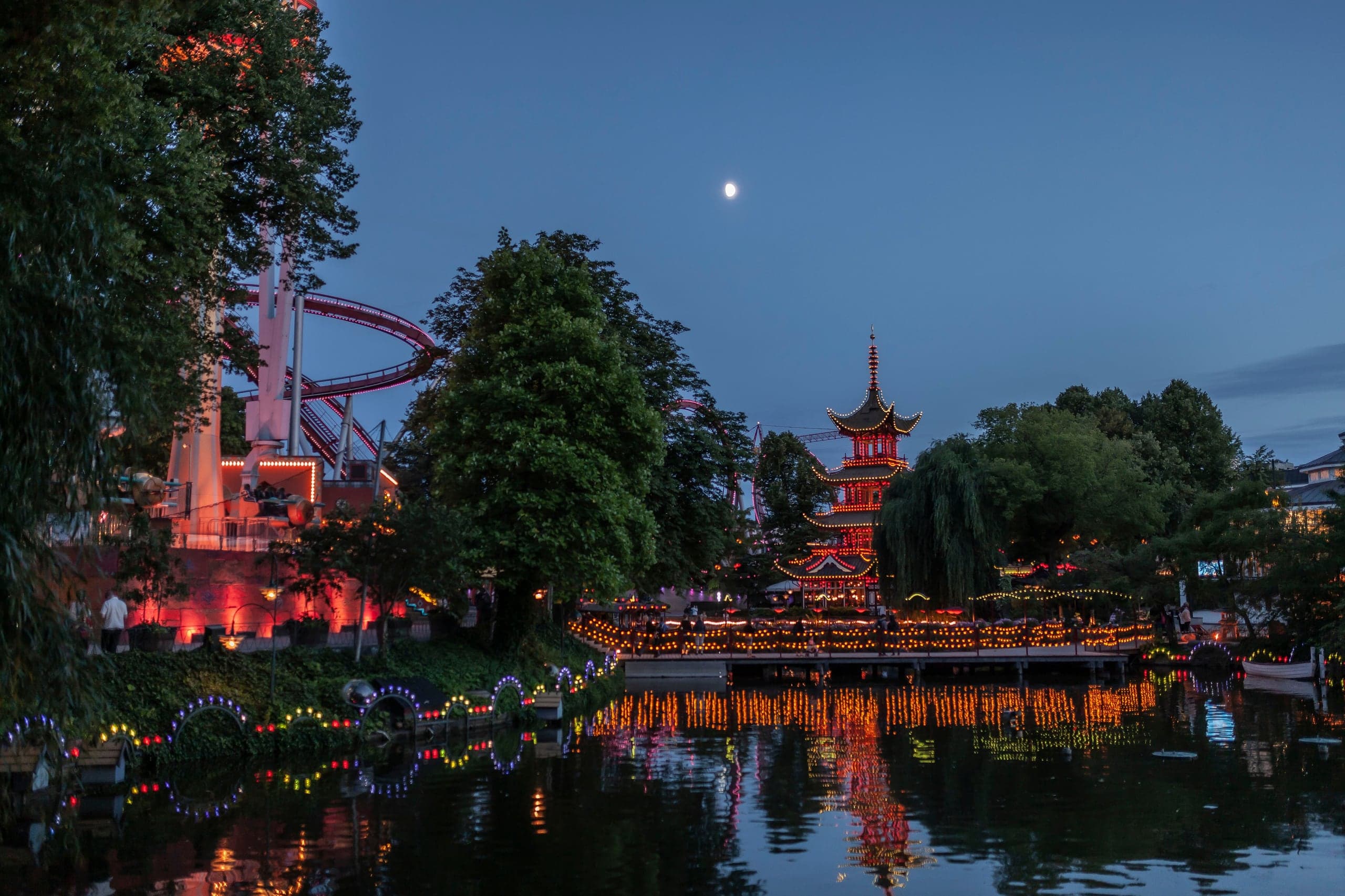 Tivoli Gardens glowing red and gold around its lake beneath a moonlit Copenhagen sky