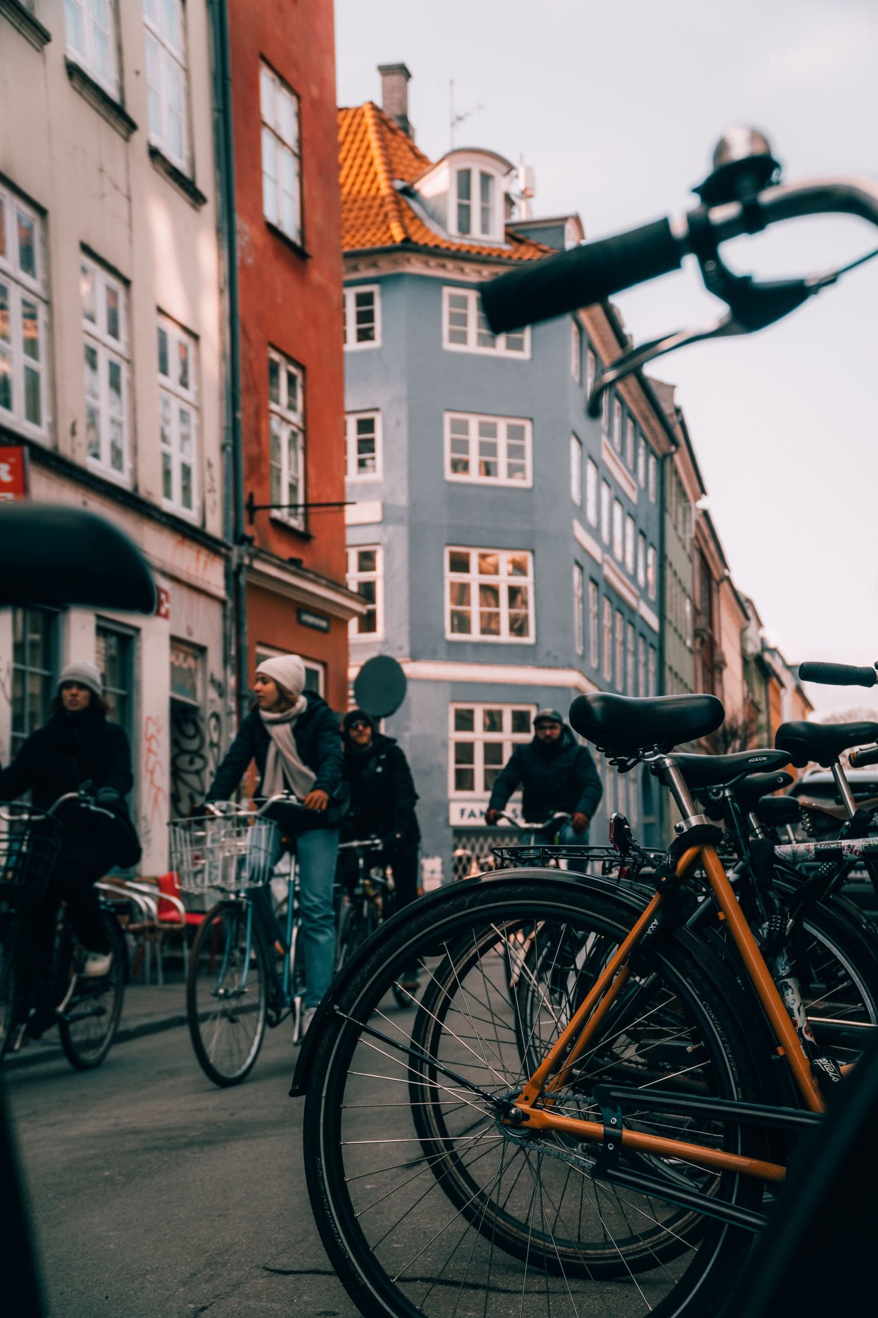 Cyclists flowing through a narrow Copenhagen street between warm red and blue historic facades