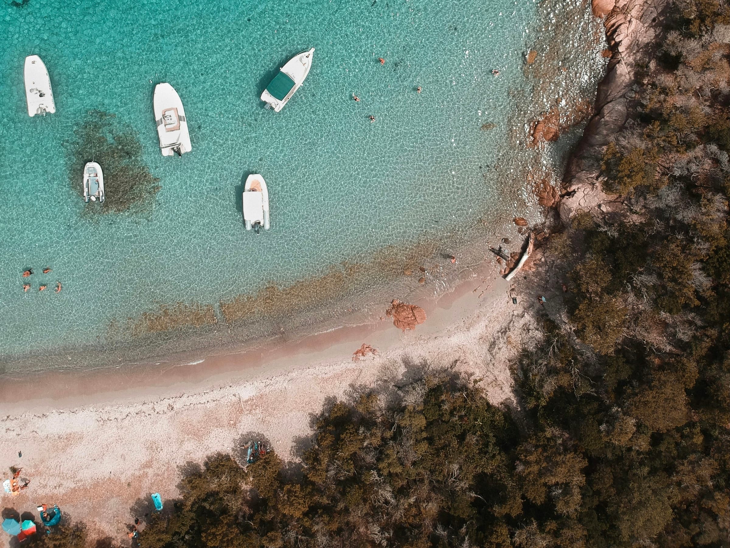 Small boats scattered across luminous turquoise water along the Corsican coast