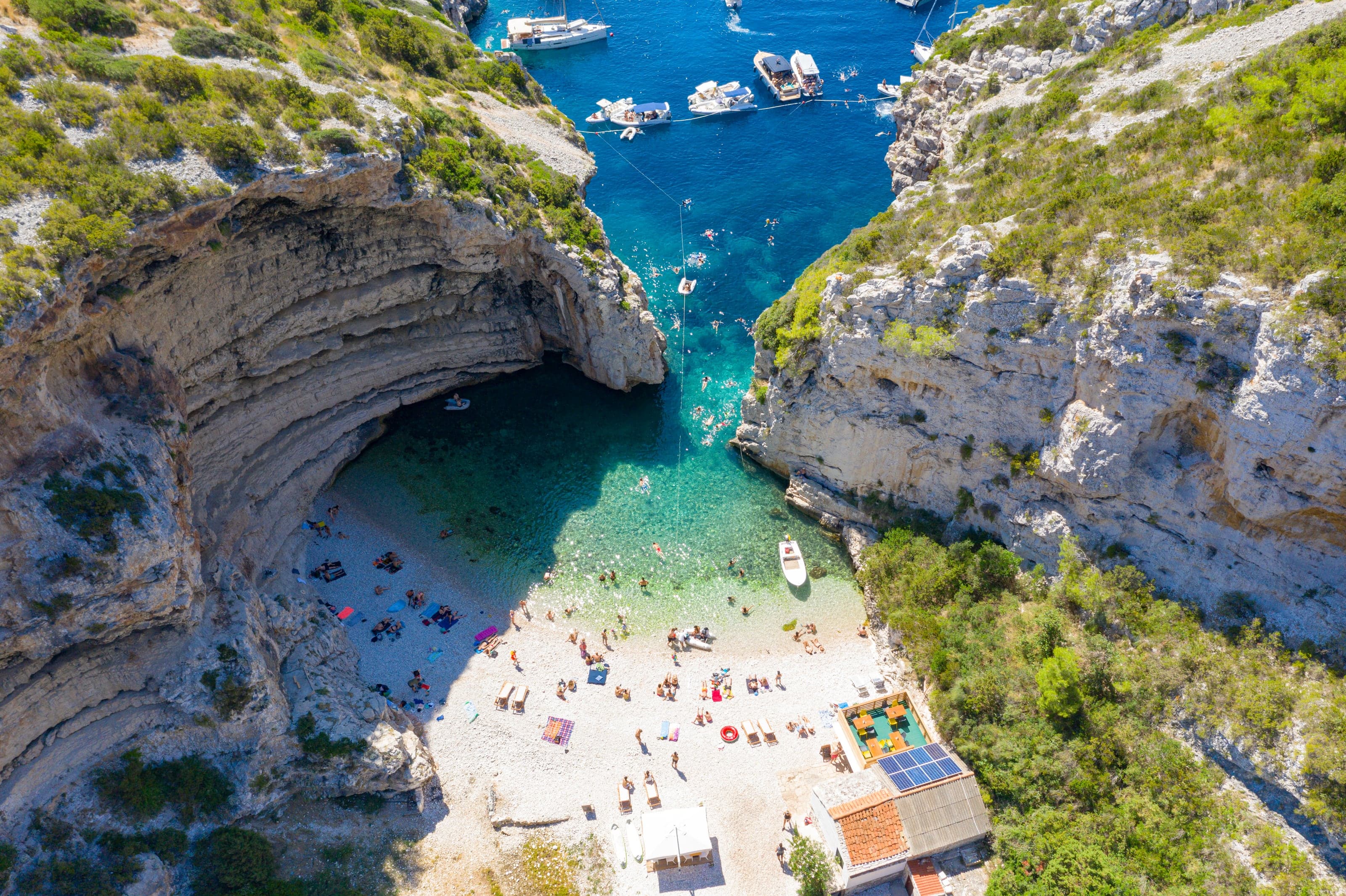 Aerial view into Stiniva's turquoise cove enclosed by pale limestone cliffs on Vis
