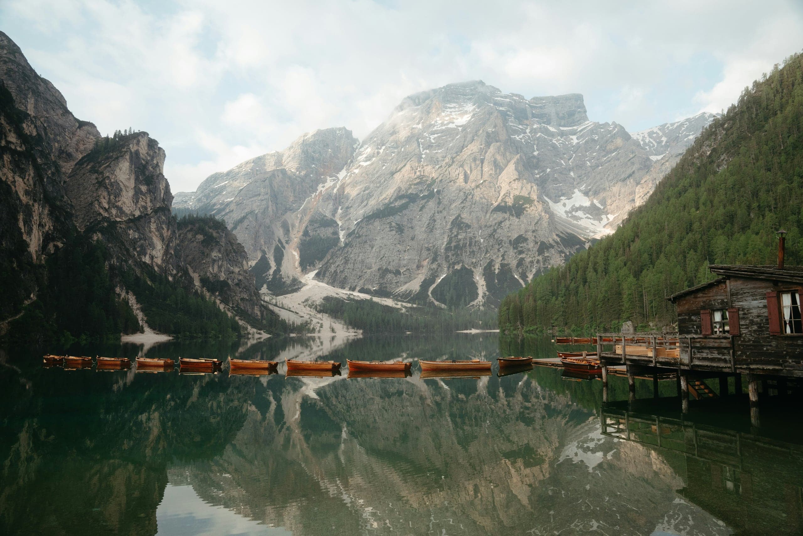 Lago di Braies at sunrise with the boathouse, wooden boats, and reflected Croda del Becco massif