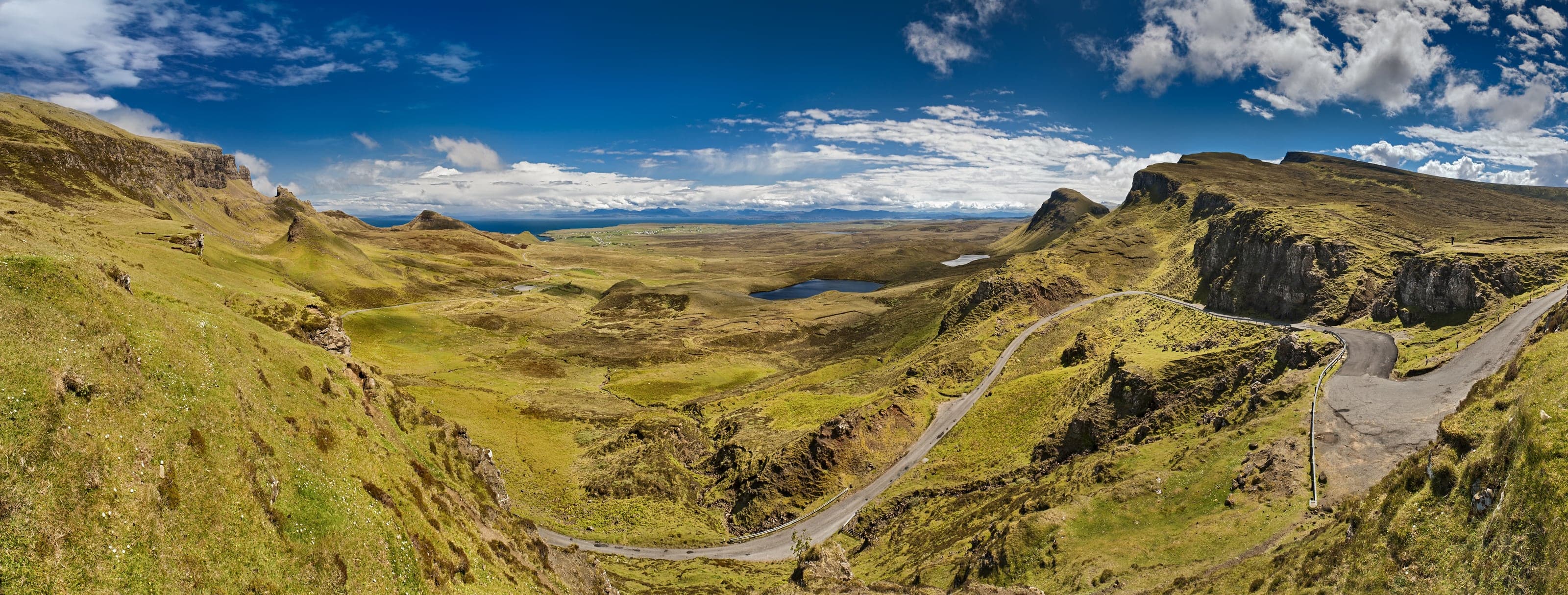 The winding Quiraing road threading between green ridges and basalt outcrops toward the distant sea