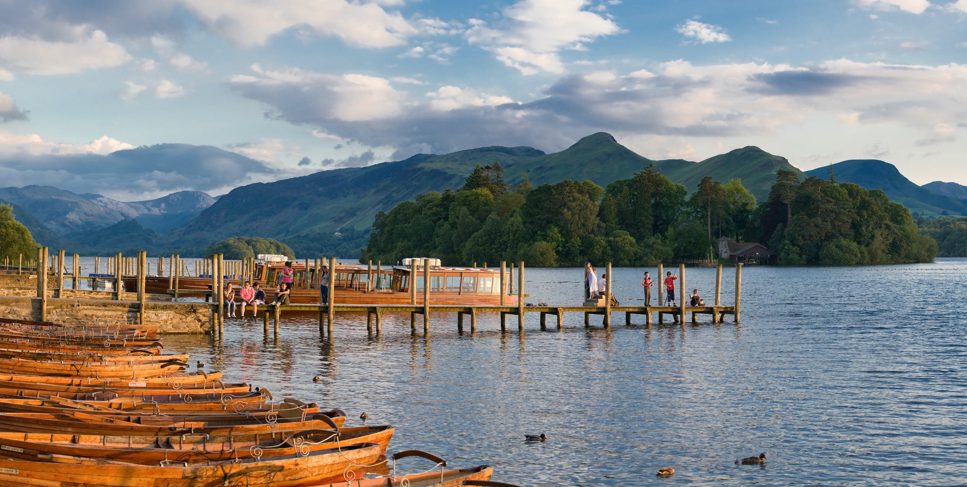 Wooden launches and people along the Derwent Water pier beneath the Lake District fells