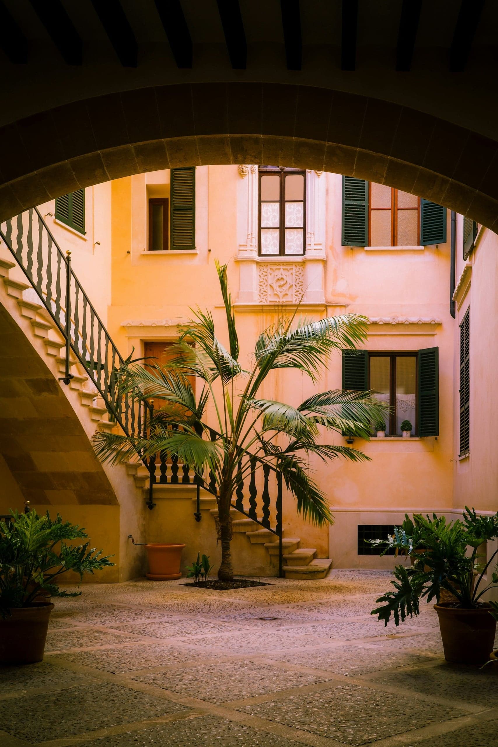 Warm peach walls, palms, and green shutters in a quiet Palma courtyard