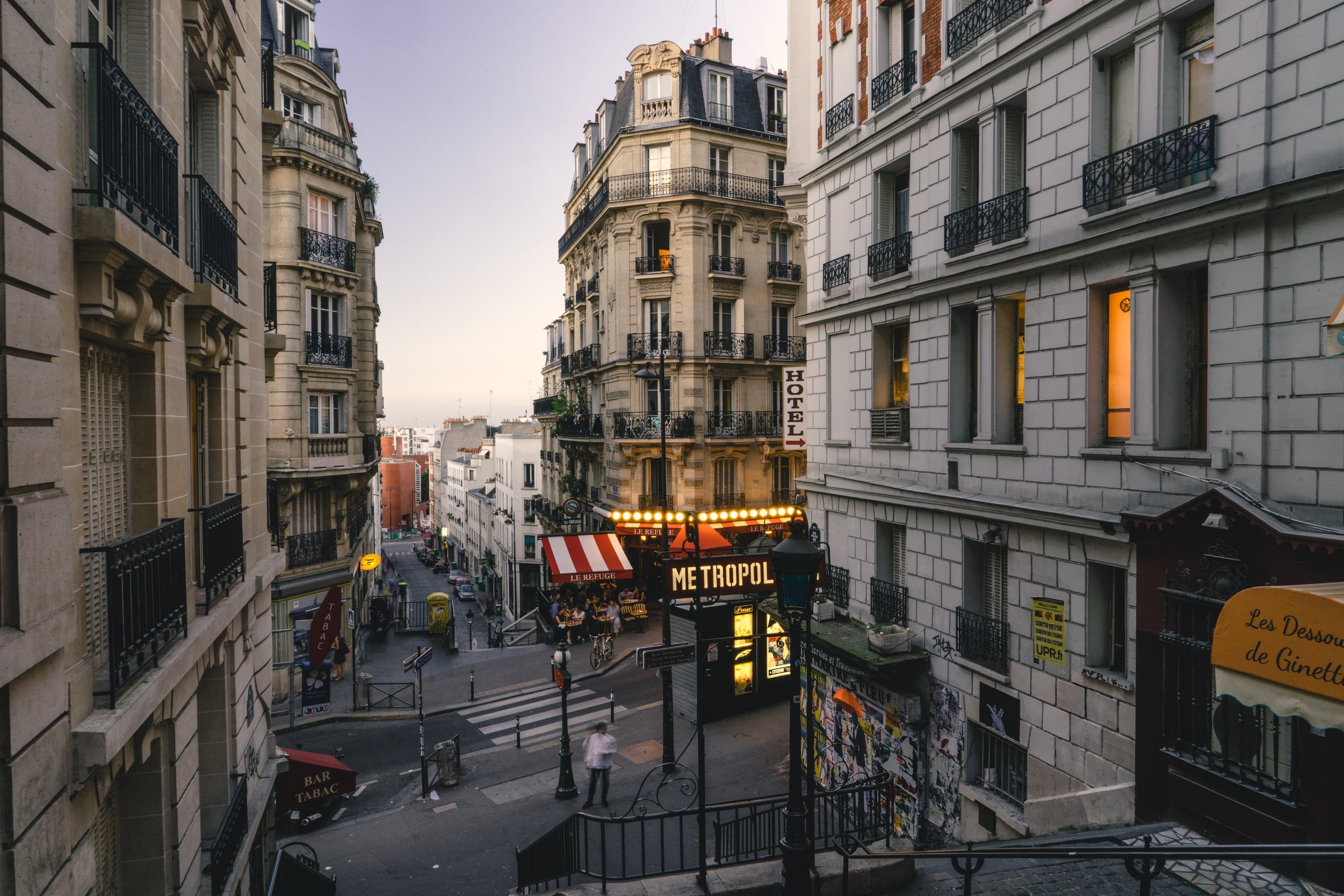 A stepped Montmartre street winding between elegant Paris facades as café lights glow at dusk