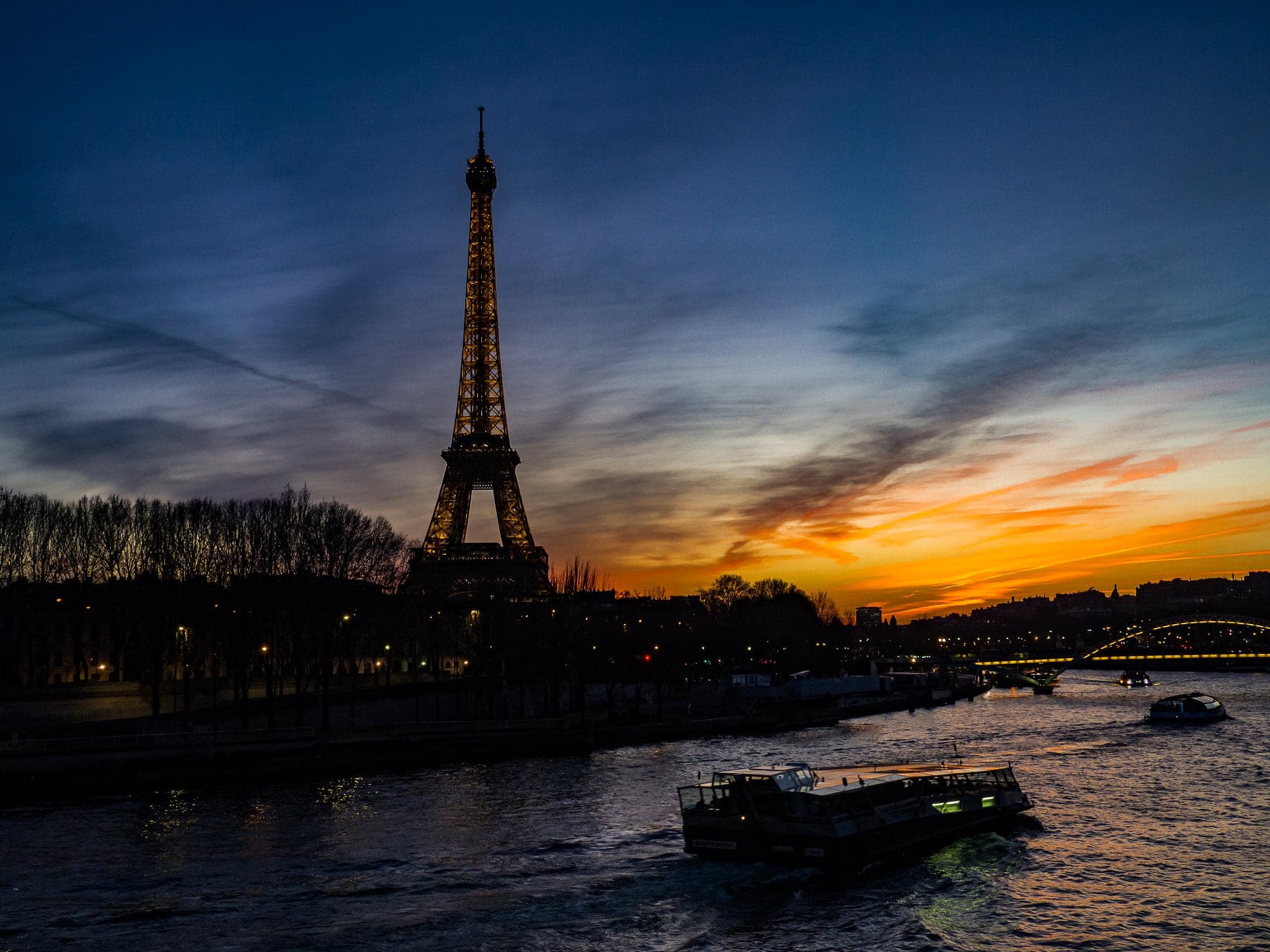 Eiffel Tower silhouetted above the Seine at a vivid blue-hour sunset