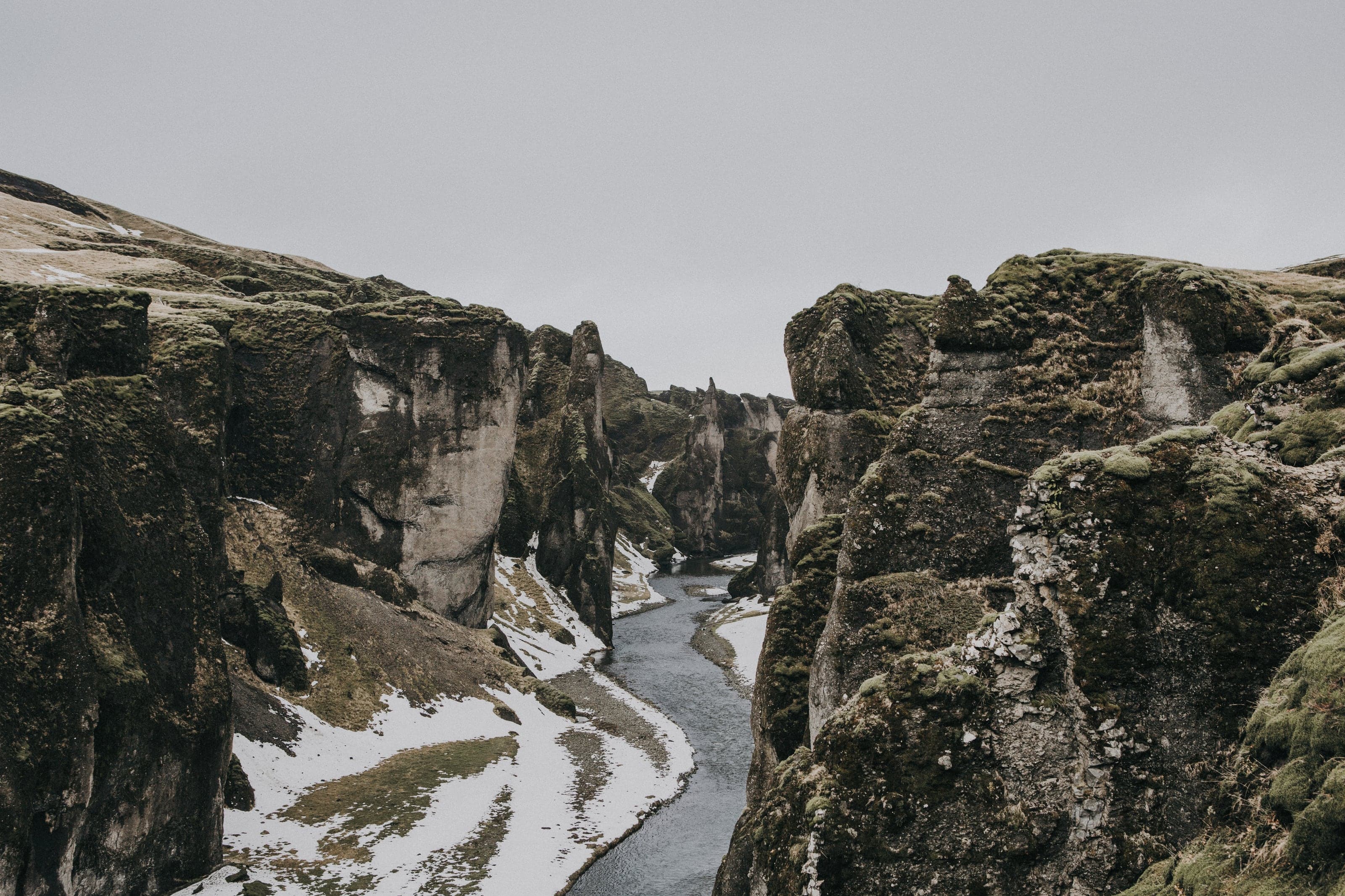 A silver river winding between sheer moss-covered walls in Iceland's Fjaðrárgljúfur canyon