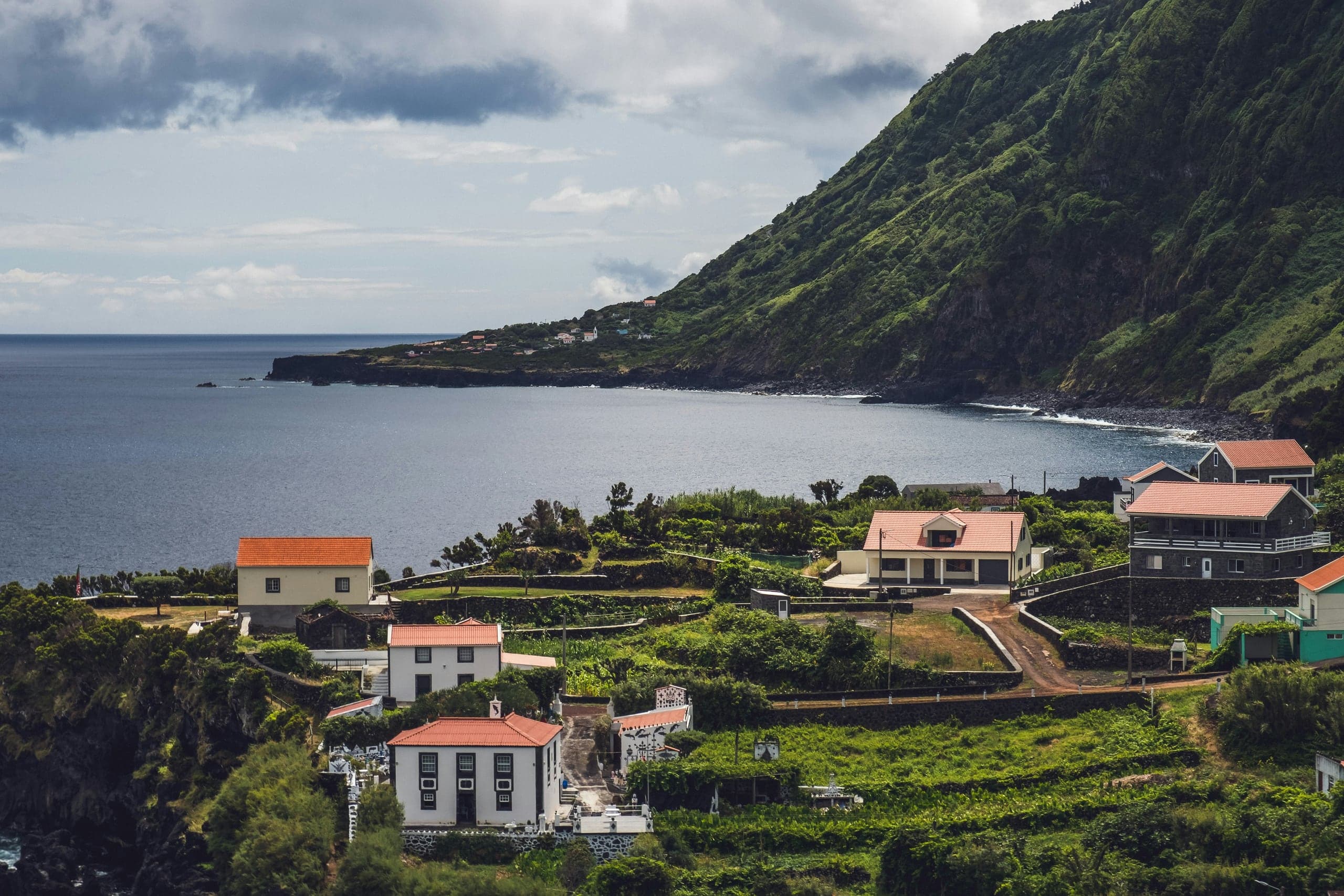 A compact oceanfront fajã village beneath São Jorge's steep green cliffs